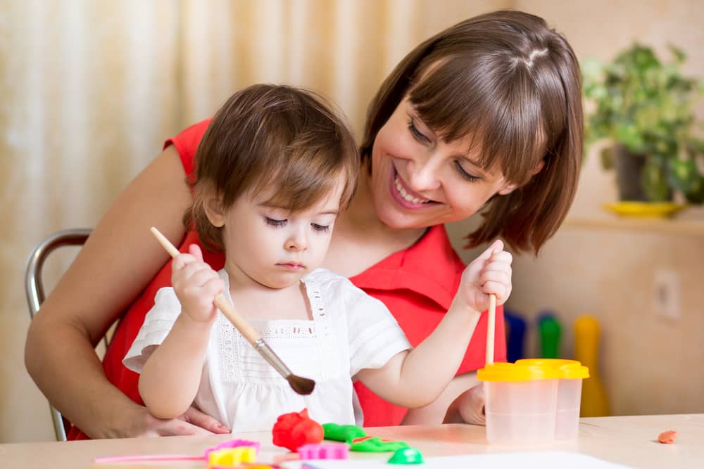 Niña y mamá jugando con plastilina en casa